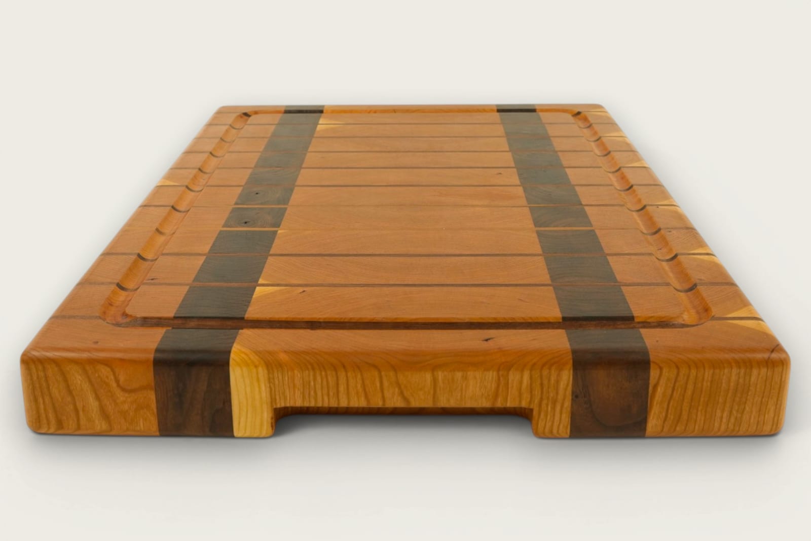 Cherry and walnut chopping block with vertical end-grain pattern, warm amber tones, and recessed handles.